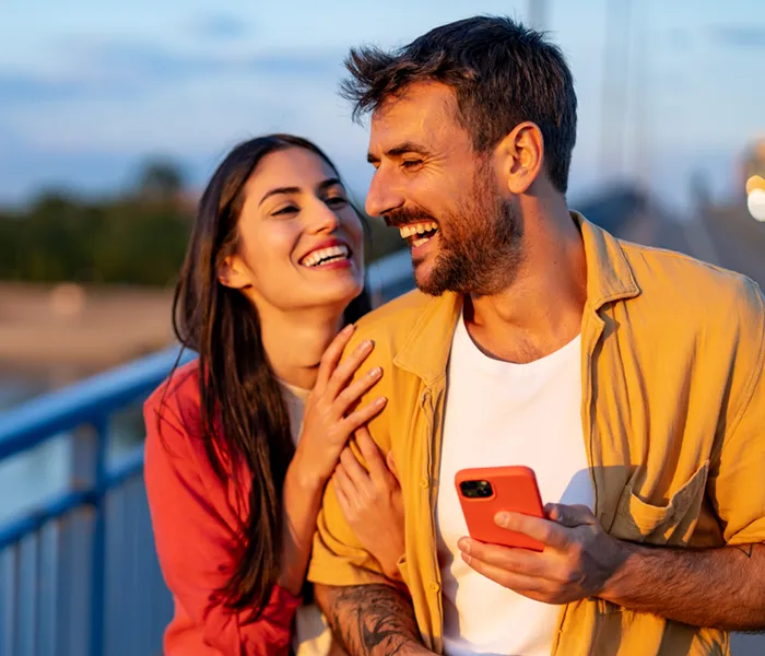 Laughing couple on a bridge with a phone at sunset